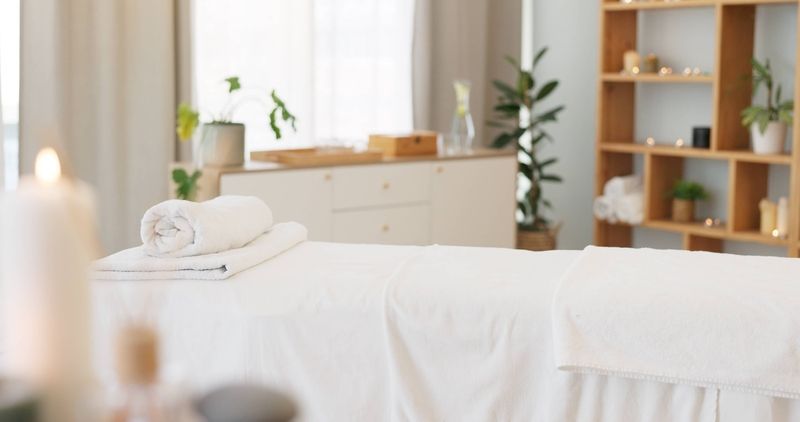 Massage table with folded towels in a bright room with plants and wooden furniture